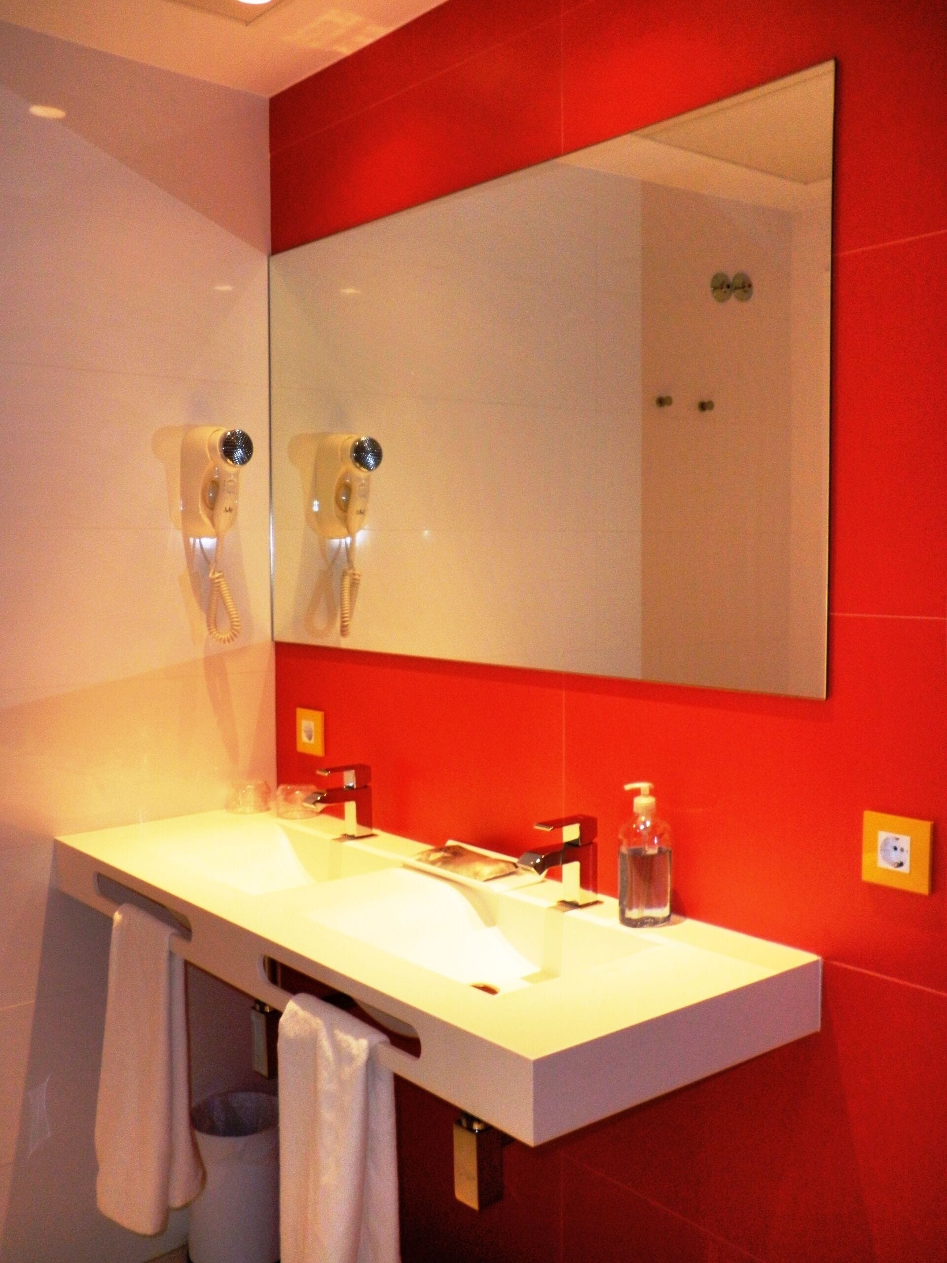 A bathroom with a white sink, a mirror, and red walls.