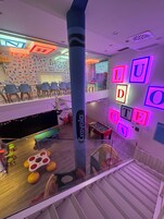 Un vestíbulo de hotel con mesa de billar, letras de neón coloridas en la pared y un pilar con la marca Crayola.