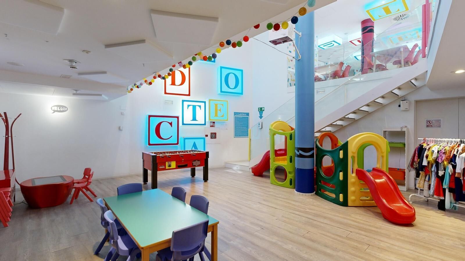 Un espace de jeux pour enfants avec un baby-foot, des structures colorées et un portant à vêtements.