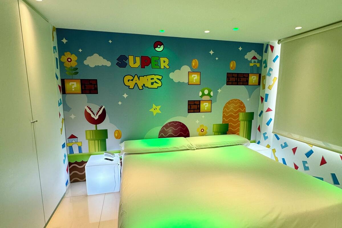 Un dormitorio con una cama, una pared con el texto 'SUPER GAMES' y una ventana con cortinas.