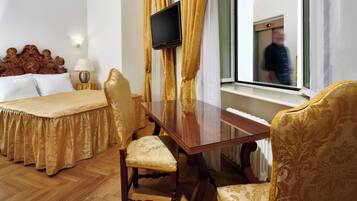 A hotel room with a bed, a desk, two chairs, a TV, and a window with a view of a building.