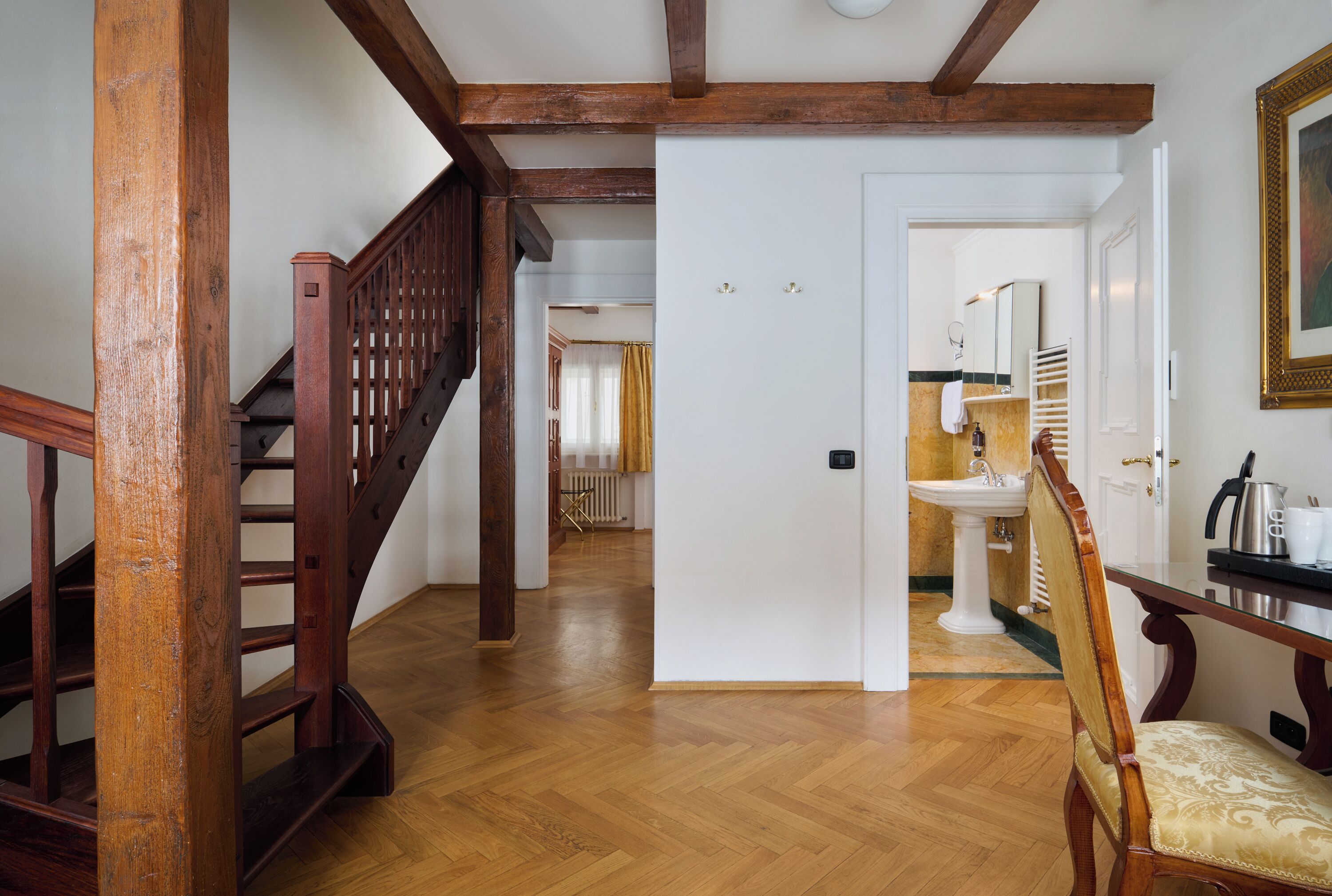 Un escalier en bois mène à une pièce dotée d’une porte blanche, d’un lavabo et d’une chaise.