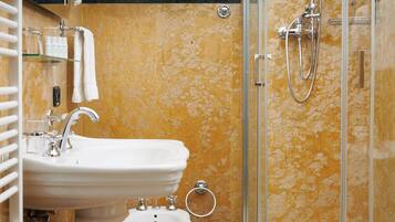 Un baño con lavamanos pedestal, un bidé, inodoro y ducha con mampara de vidrio.