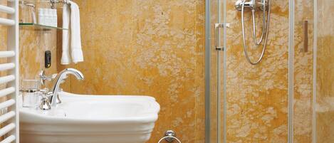 Un baño con lavamanos pedestal, un bidé, inodoro y ducha con mampara de vidrio.