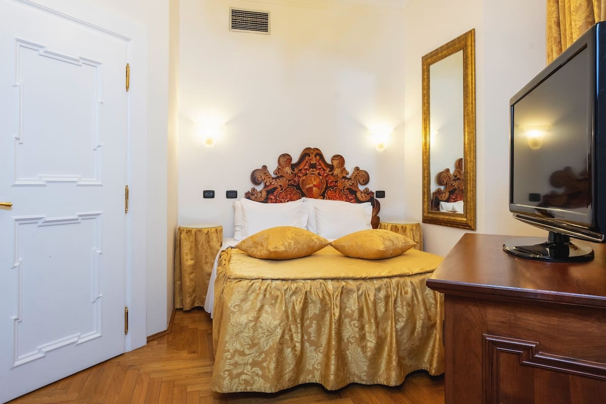 Een hotelkamer met een groot bed, een televisie op een houten dressoir en een witte deur.