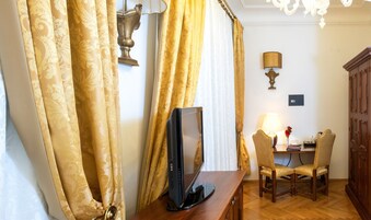 Quarto de hotel com escrivaninha de madeira, duas cadeiras, um computador e uma luminária.