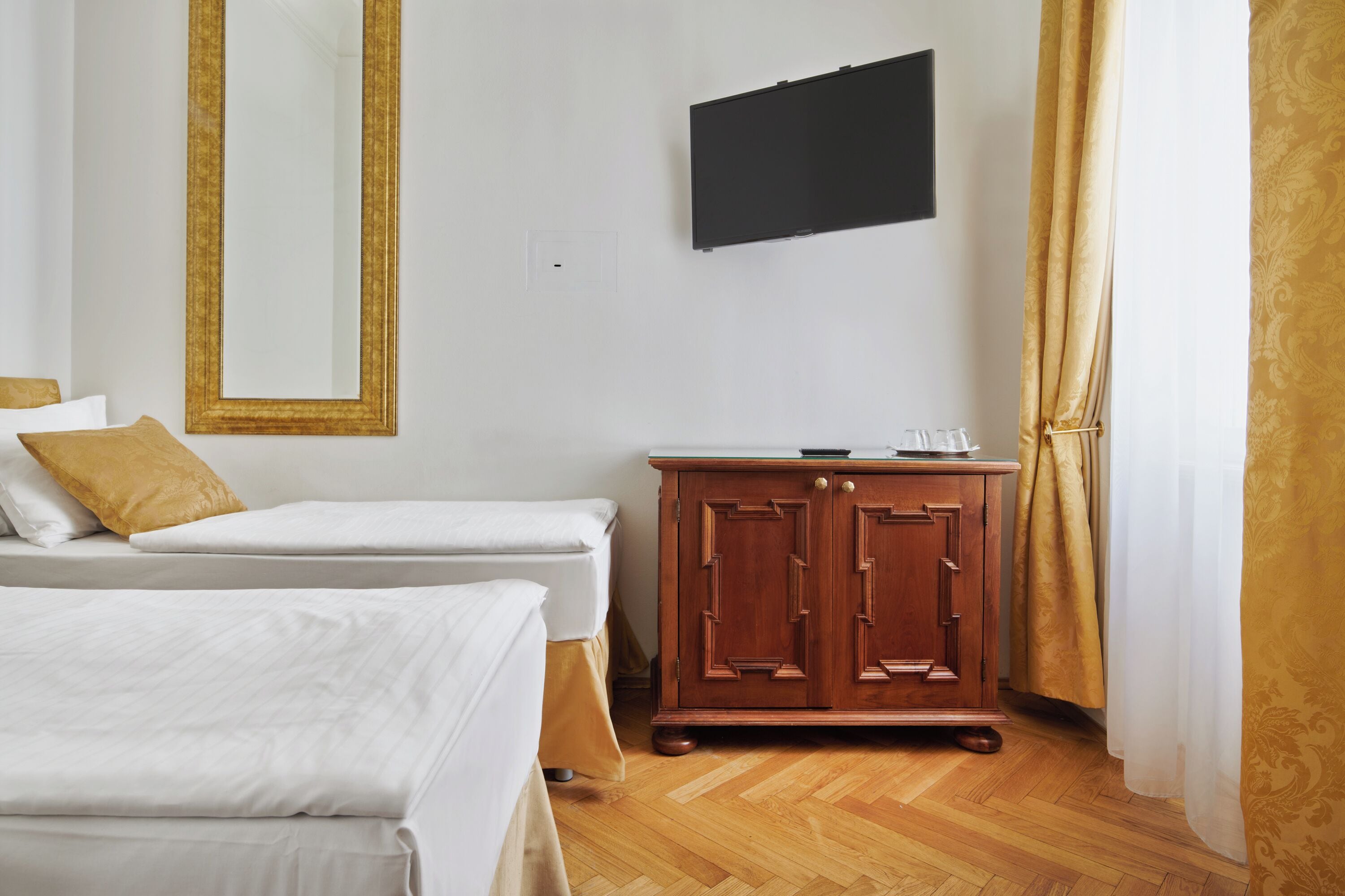Ein Hotelzimmer mit zwei Betten, einem Holzschrank, einem Flachbildfernseher und einem Fenster mit Vorhängen.