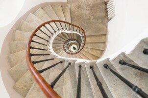 Escadaria em espiral com corrimão de madeira e degraus de pedra.
