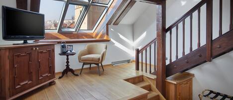 A loft-style room with a wooden staircase, a television, a chair, and a view of the city through skylights.