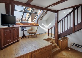 Un loft con scala in legno, televisore, una poltrona e vista sulla città tramite finestrature.