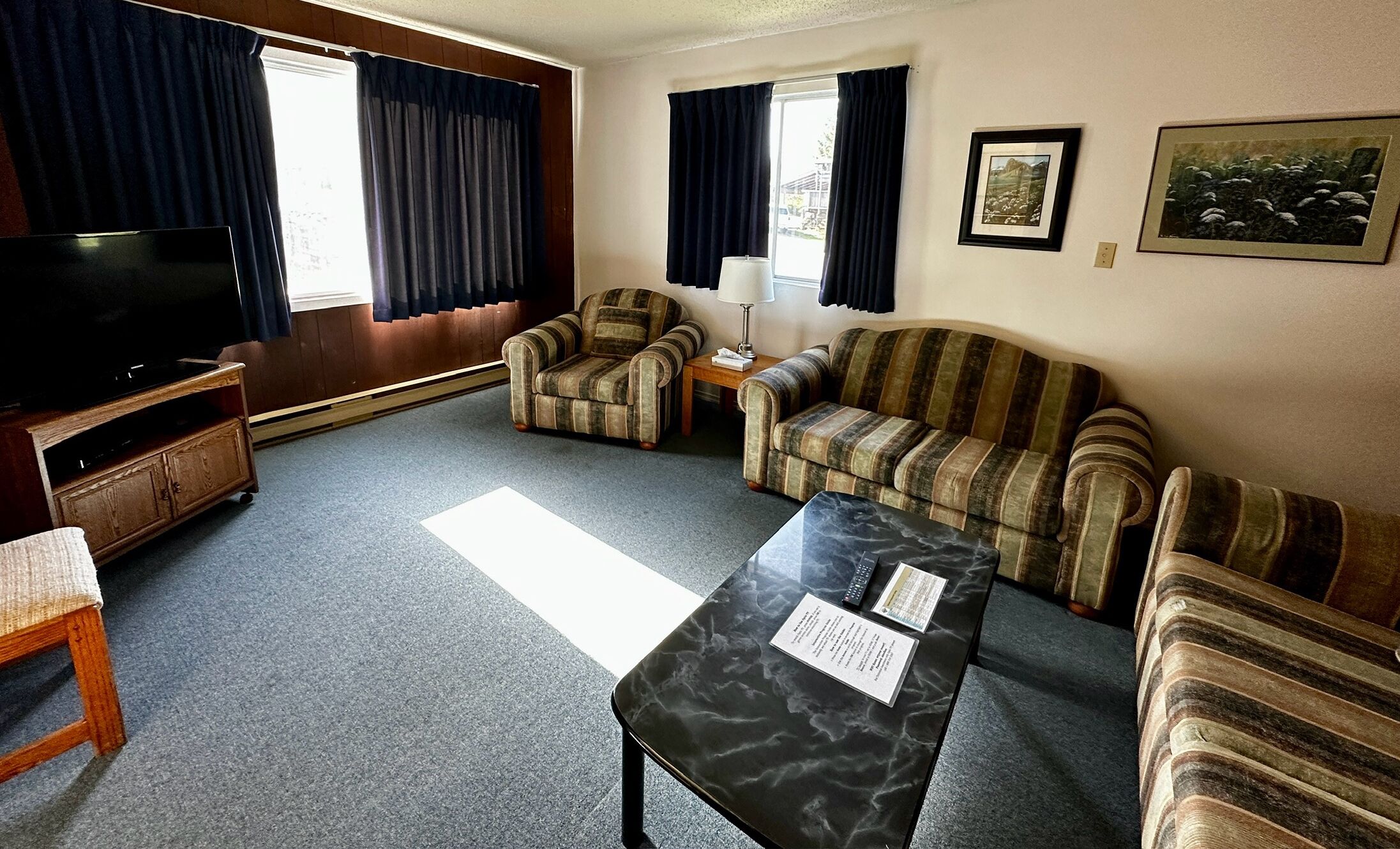 A living room with a television, two striped armchairs, a sofa, a marble coffee table, and a small side table with a lamp.