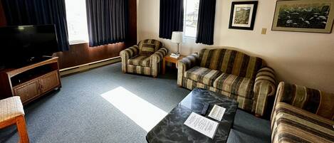A living room with a television, two striped armchairs, a sofa, a marble coffee table, and a small side table with a lamp.