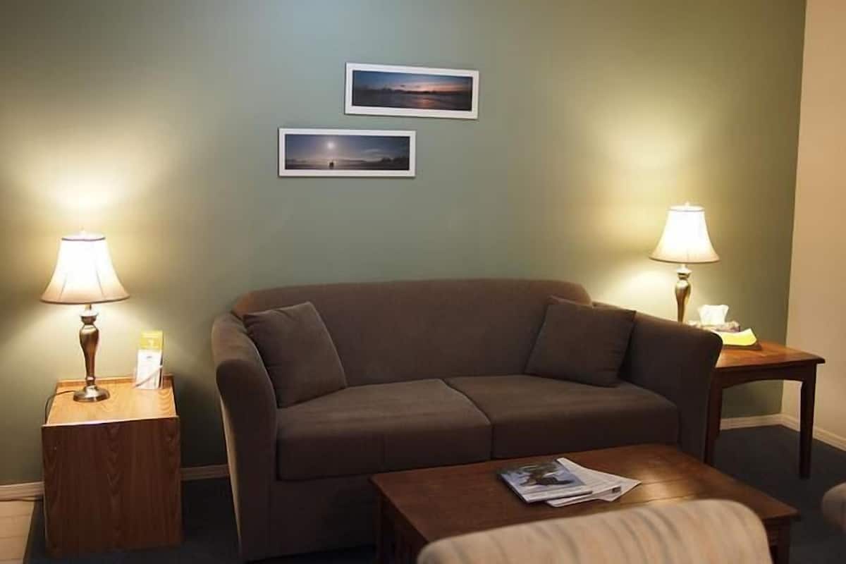 A living room with a brown sofa, two side tables with lamps, and two framed pictures on the wall.