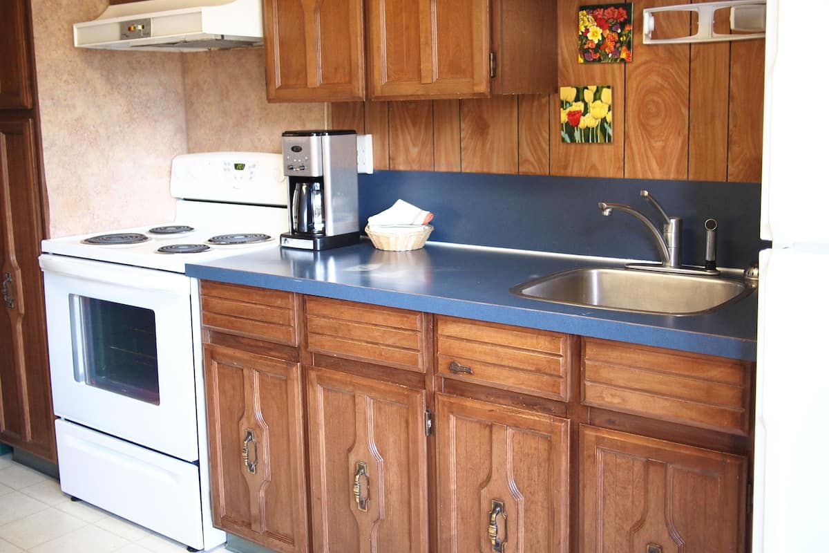 A kitchen with wooden cabinets, a white stove, a coffee maker, and a sink.