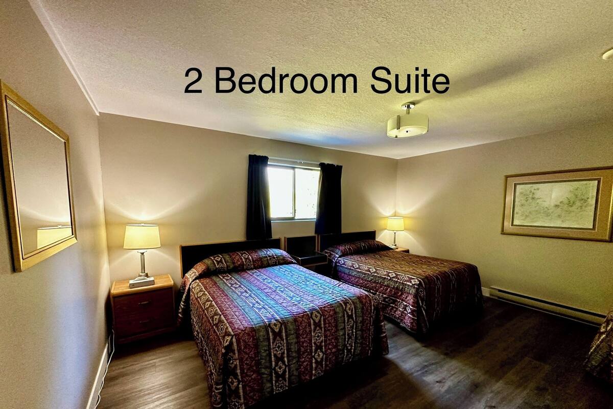 A 2 bedroom suite with two beds, nightstands, lamps, a window, and a framed picture on the wall.
