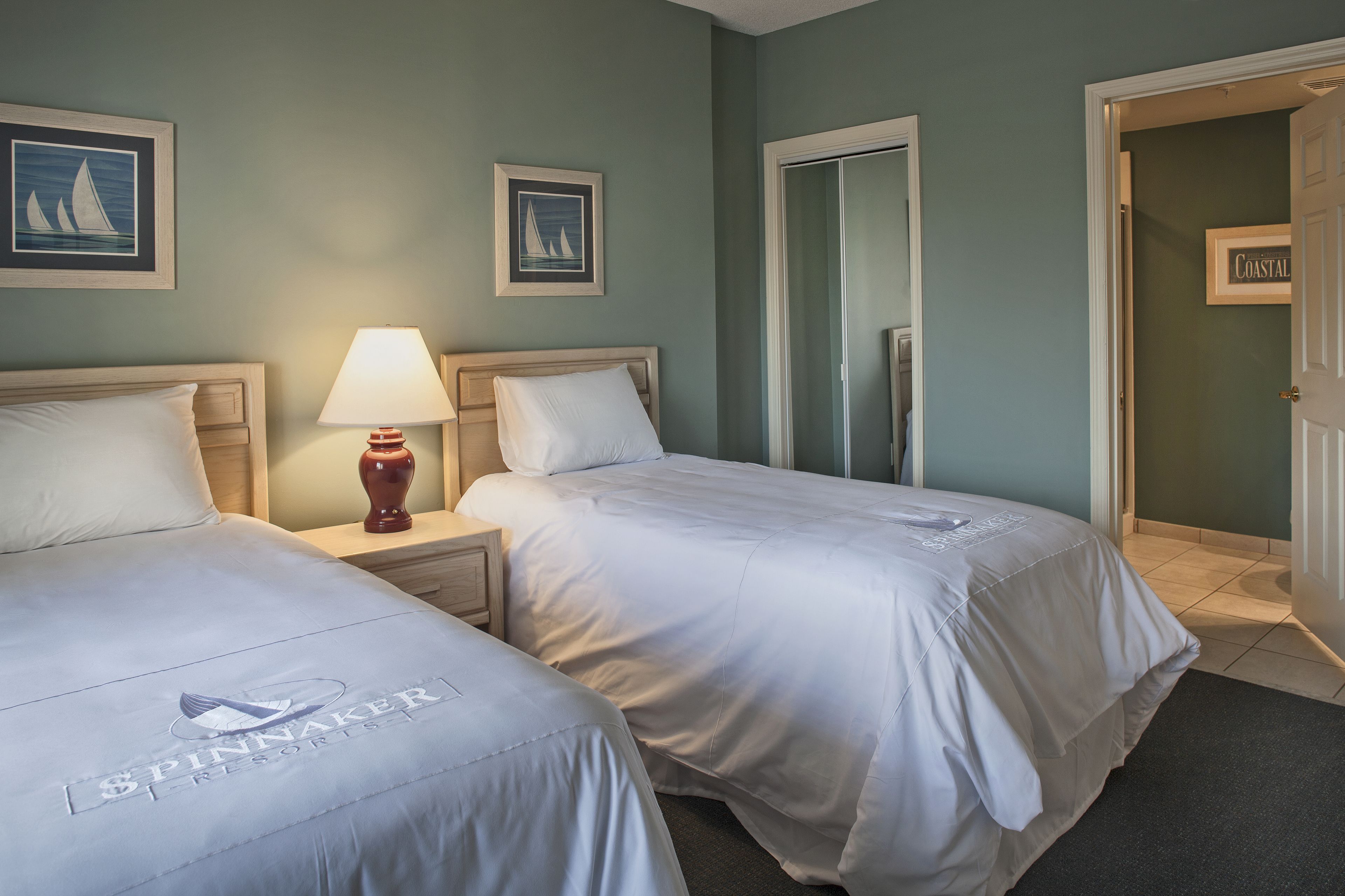 Een hotelkamer met twee bedden, een nachtkastje met een lamp en een deur naar een badkamer.