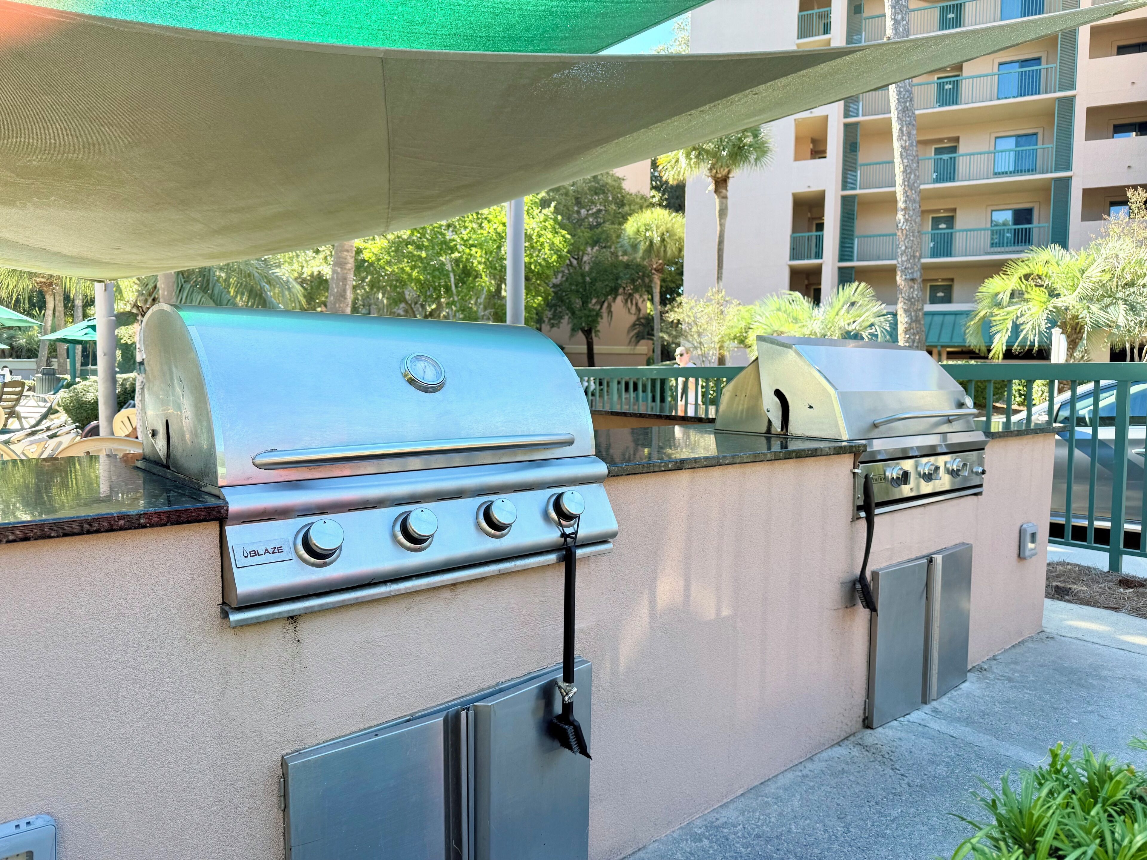Ein Grillbereich im Freien mit einem Blaze-Gasgrill und einem eingebauten Backofen, umgeben von einer Beton-Terrasse und einer grünen, baumbestandenen Überdachung.