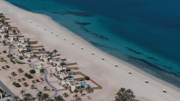 An aerial view of a resort with multiple bungalow-style accommodations, a sandy beach, and a clear blue sea. - Anantara Sir Bani Yas Island Al Yamm Villa Resort (Sir Bani Yas Island)