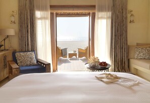 A bedroom with a large bed, a chair, a small table with a bowl of fruit, and a view of the beach through an open door. - Anantara Sir Bani Yas Island Al Yamm Villa Resort (Sir Bani Yas Island)