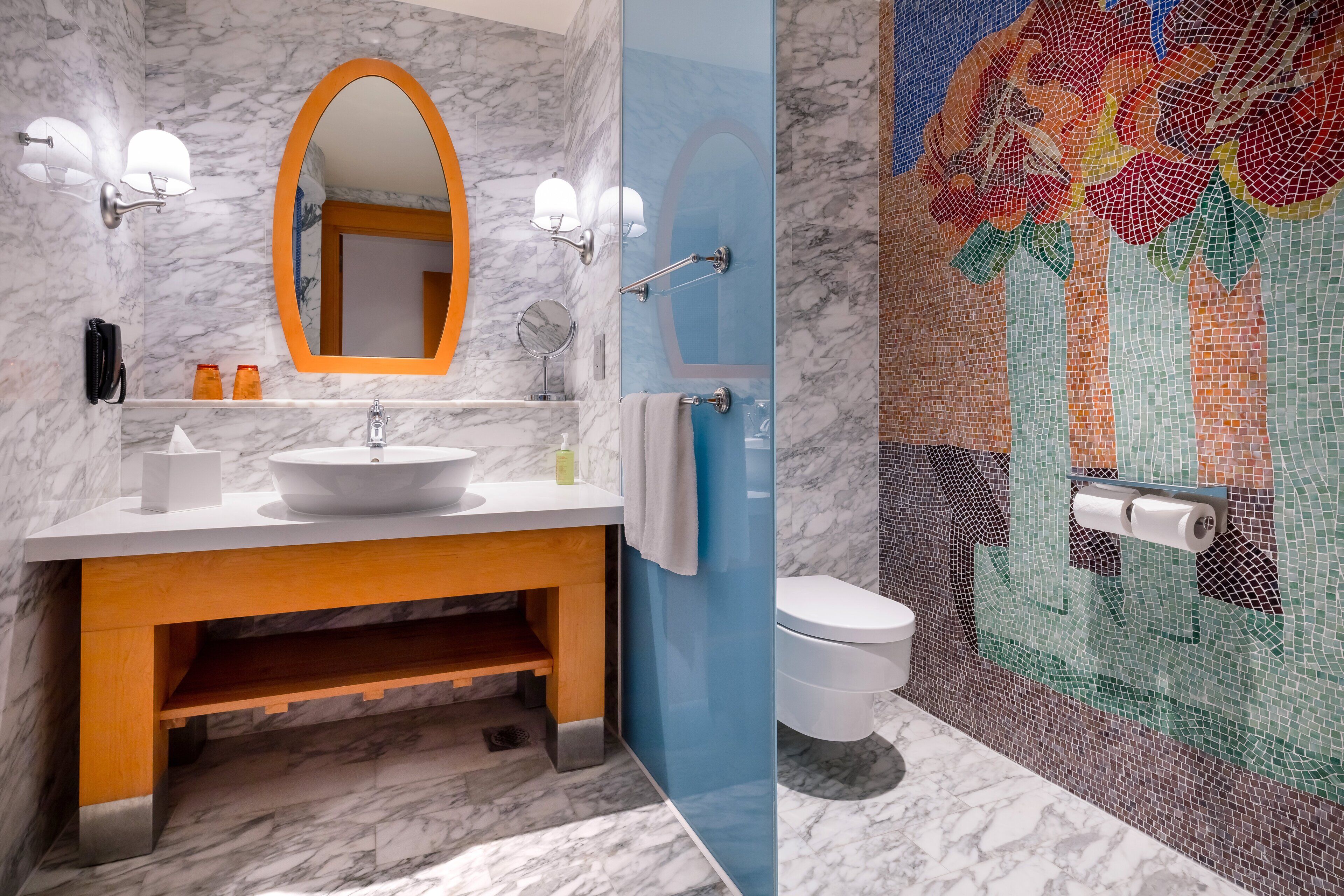 A bathroom with a marble sink, wooden vanity, a large mirror, and a mosaic wall.