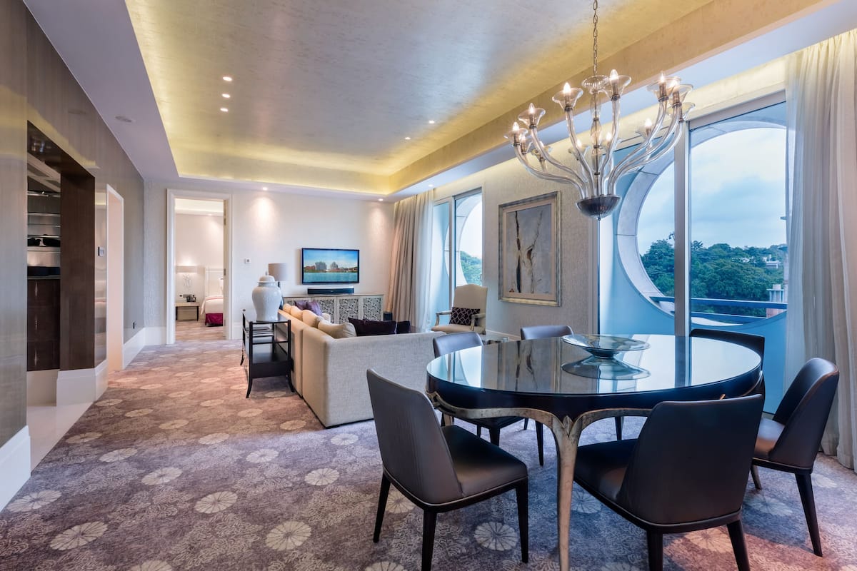 Une chambre d’hôtel moderne dotée d’un coin repas, d’un canapé, d’un lustre et d’une grande fenêtre offrant une vue panoramique.