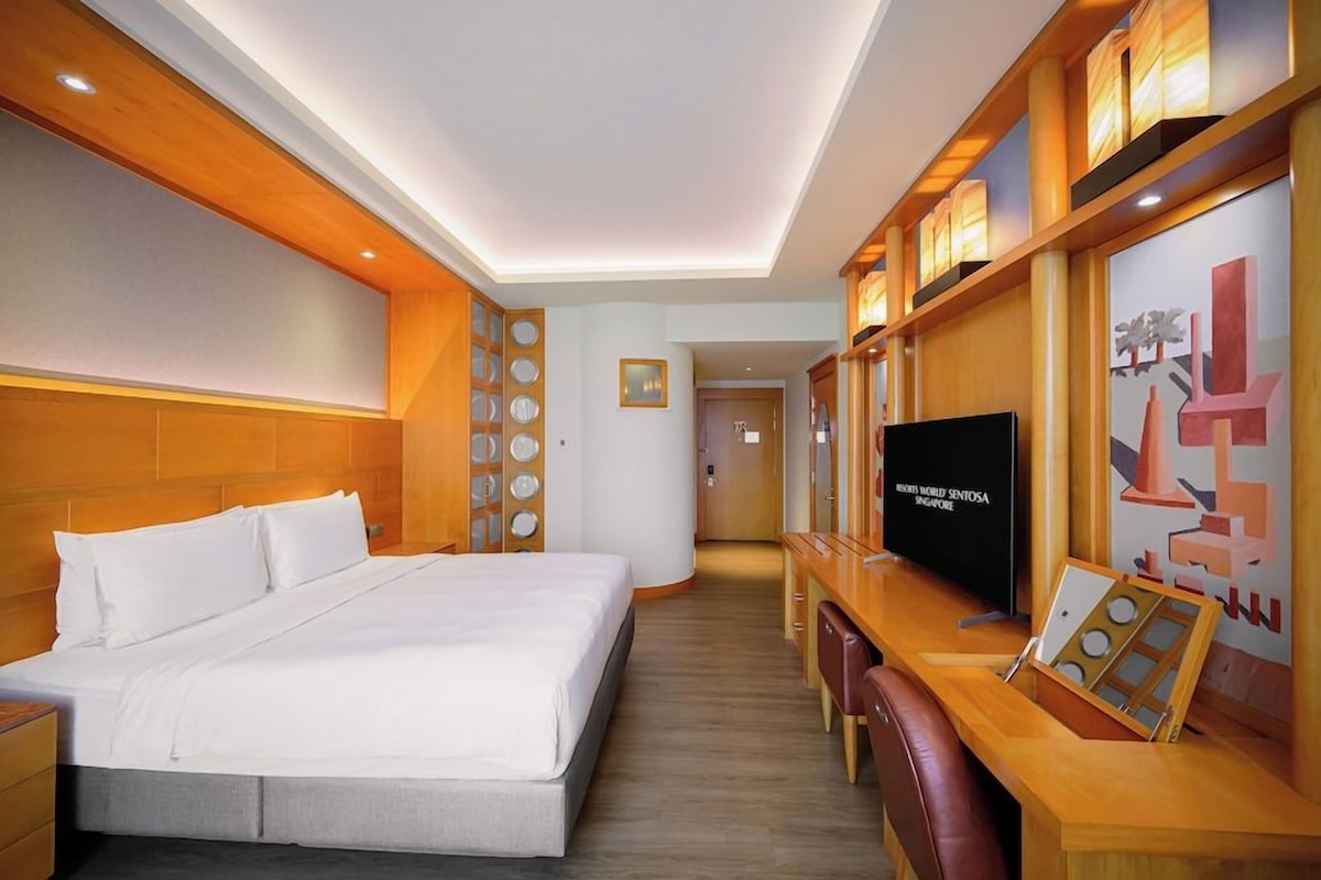 Une chambre d’hôtel avec un grand lit, un bureau avec une chaise, une télévision et un mur orné d’un tableau encadré.