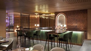 Een moderne bar met een bargedeelte, groene stoelen en een decoratieve wand.
