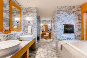 Ein modernes Badezimmer mit Marmorwänden, einem großen Spiegel, zwei Waschbecken, einem Holzschrankenbau und einer Badewanne.