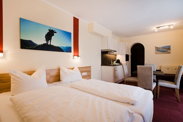 Habitación de hotel con una cama grande, un escritorio y una silla. Hay un cuadro en la pared y una ventana con vistas a las montañas.