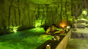 Een koppel in een spa met weinig licht, die lijkt op een grot, met een stenen muur en een houten bank.