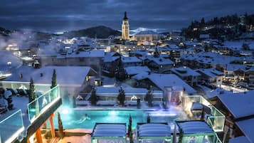 Un resort cubierto de nieve con zona de piscina, una torre del reloj y montañas al fondo.