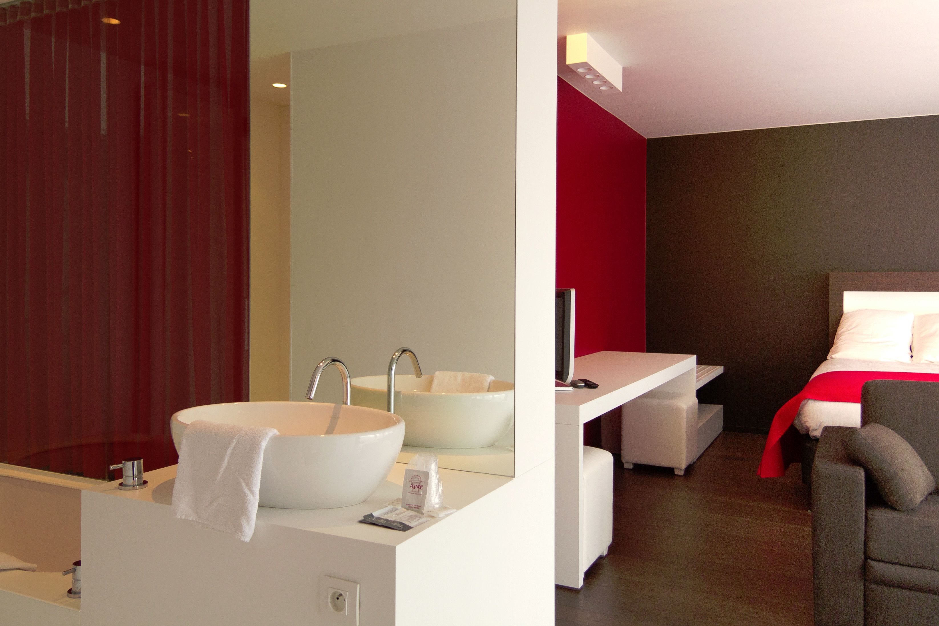 A modern bathroom with a large white sink, a mirror, and a red accent wall.