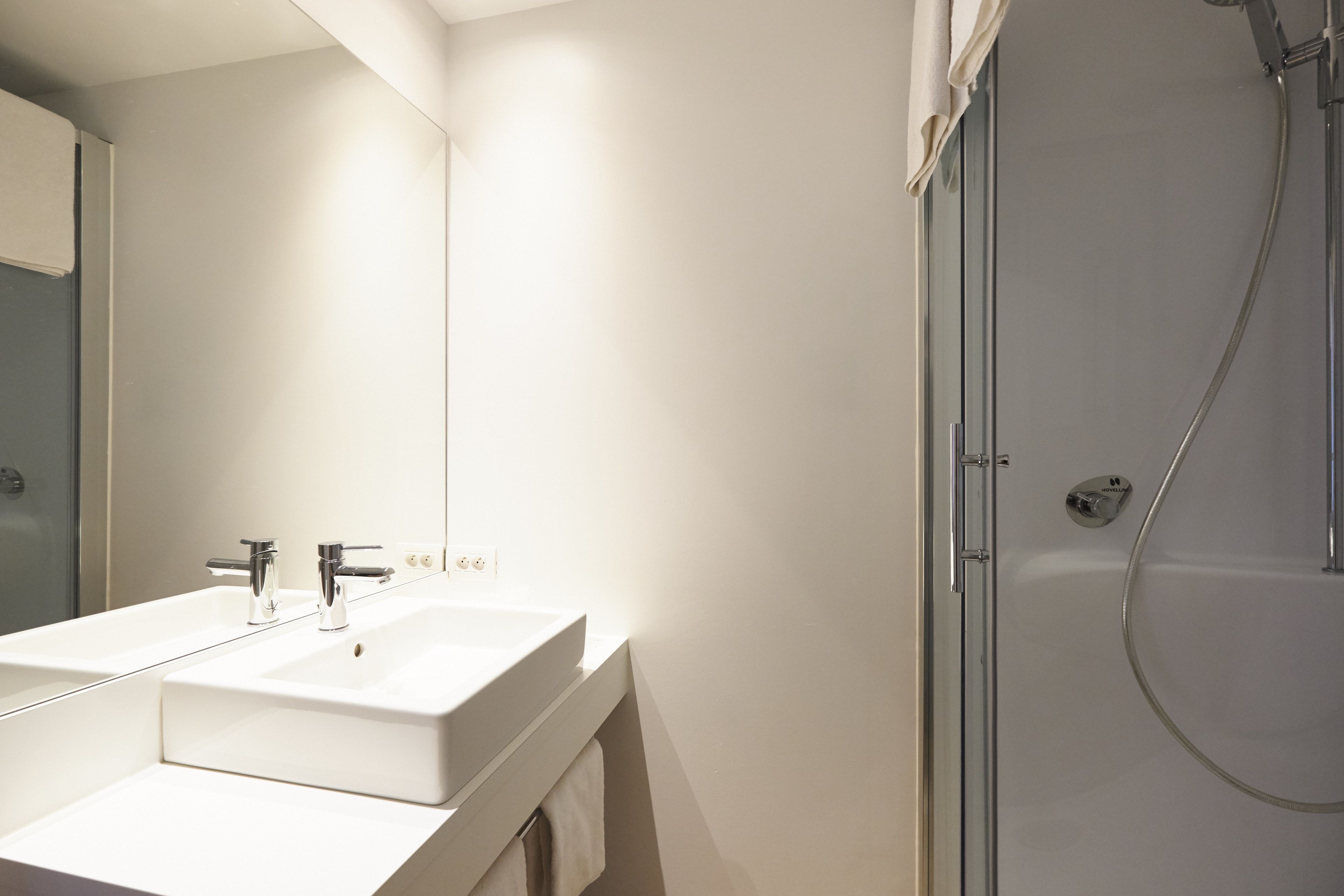 Casa de banho moderna com lavatório branco, espelho e chuveiro.