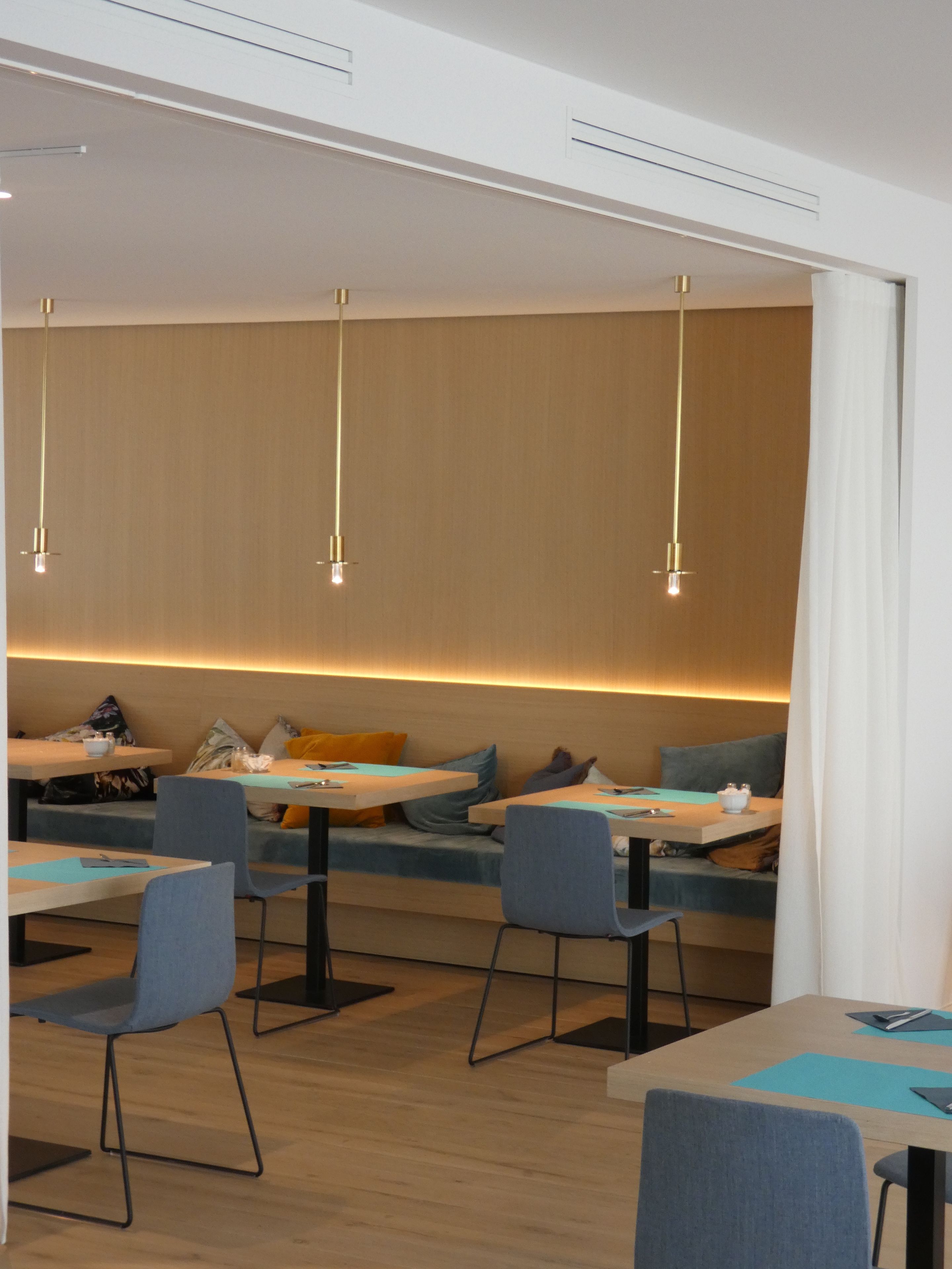 A modern dining area with tables and chairs, a long bench with cushions, and pendant lighting.
