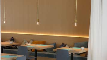A modern dining area with tables and chairs, a long bench with cushions, and pendant lighting.