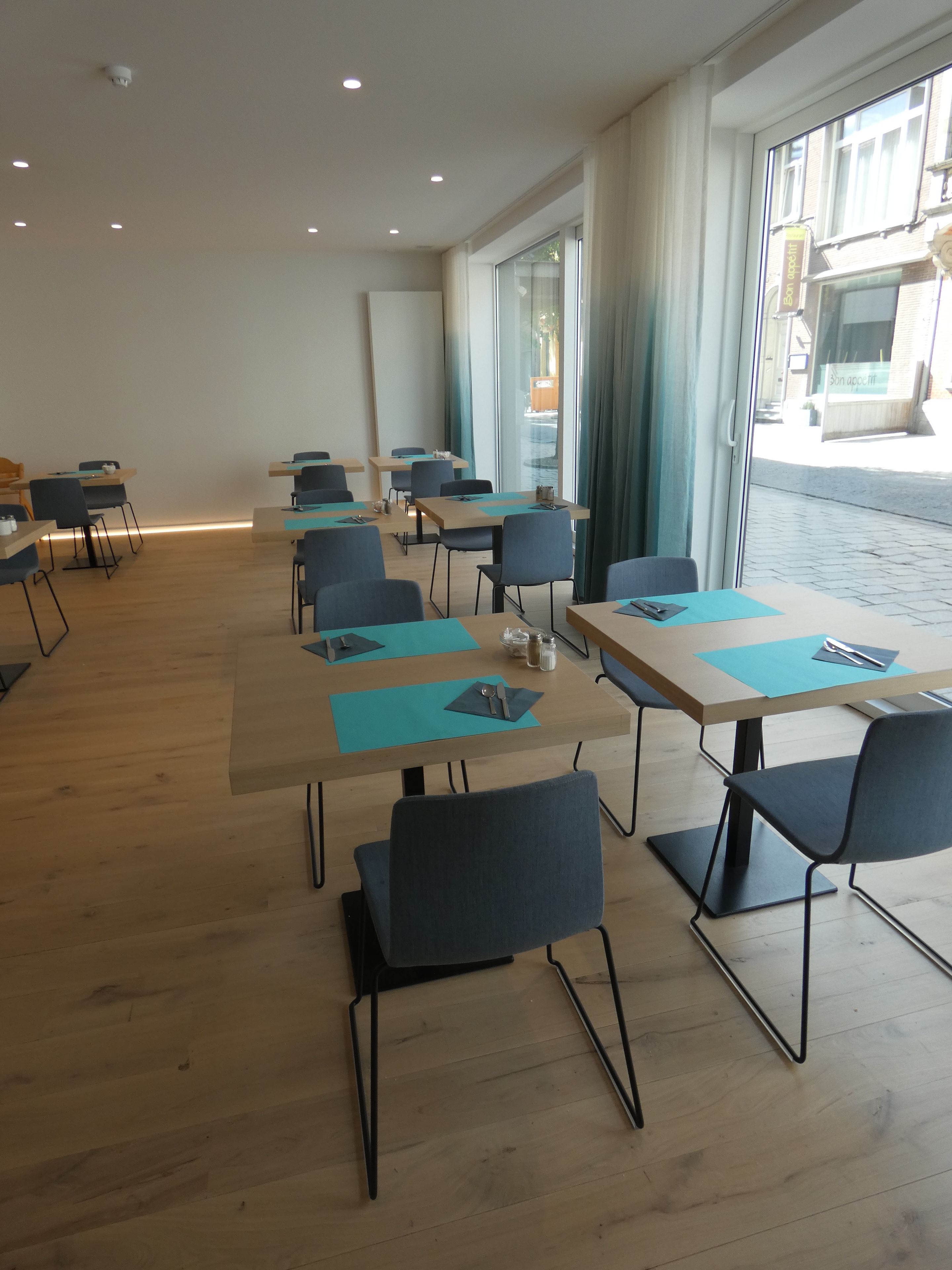 Un salón de conferencias con mesas y sillas, amplias ventanas con cortinas y vista a la calle.