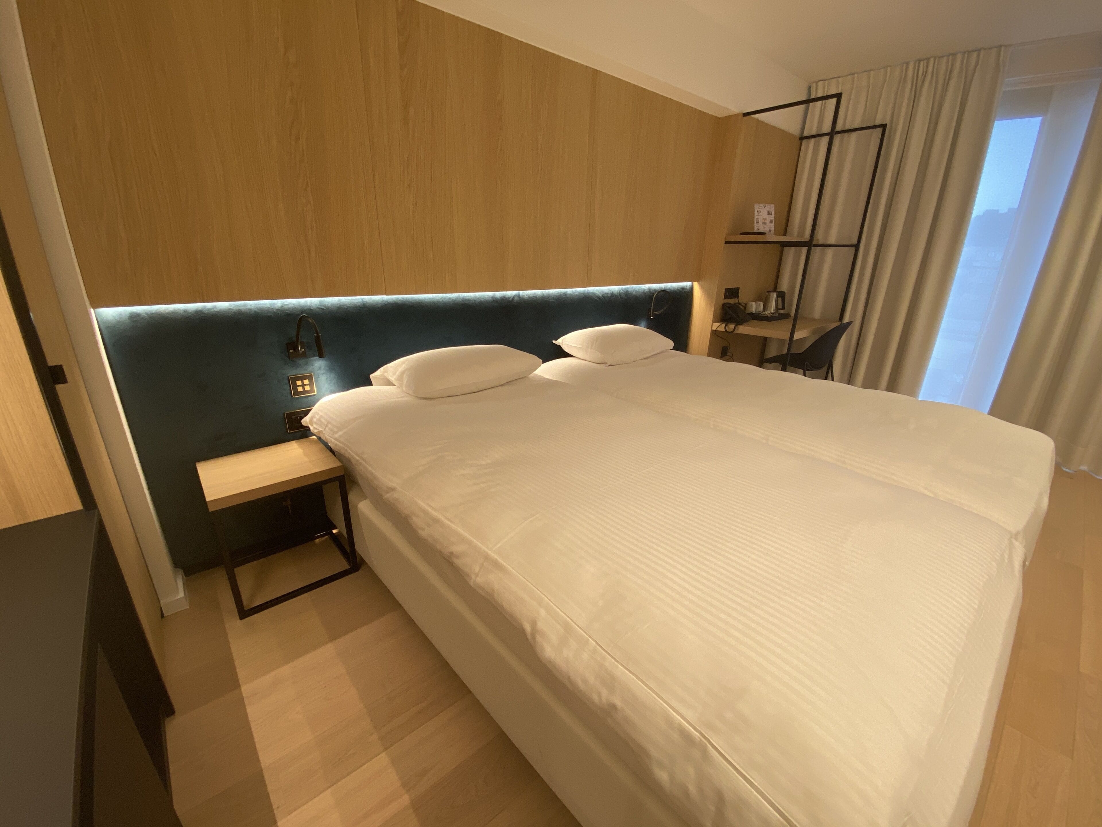 A modern hotel room with a large bed, a bedside table, a nightstand, and a headboard.