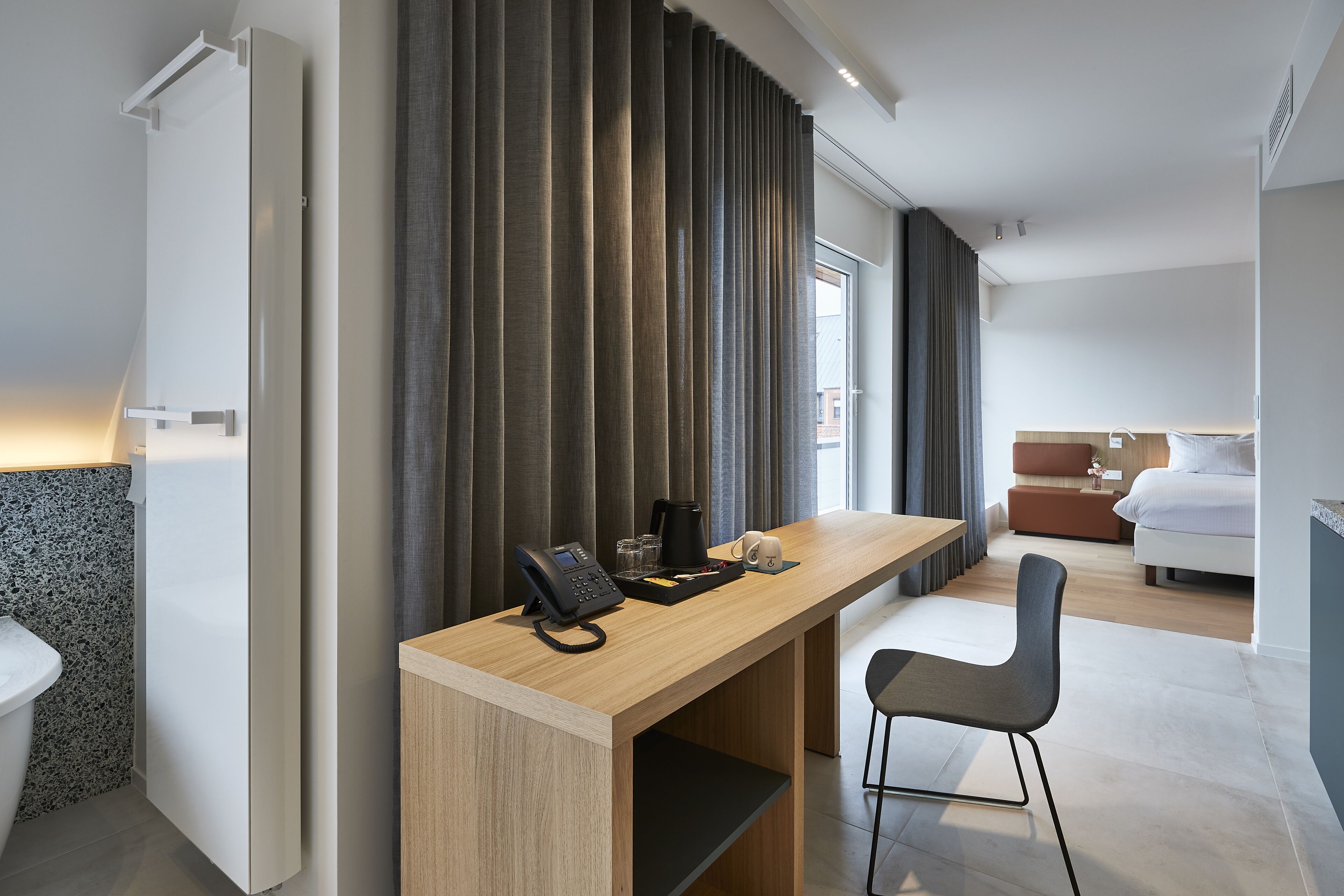Una habitación de hotel moderna con un escritorio de madera, un teléfono, una cafetera y una silla.