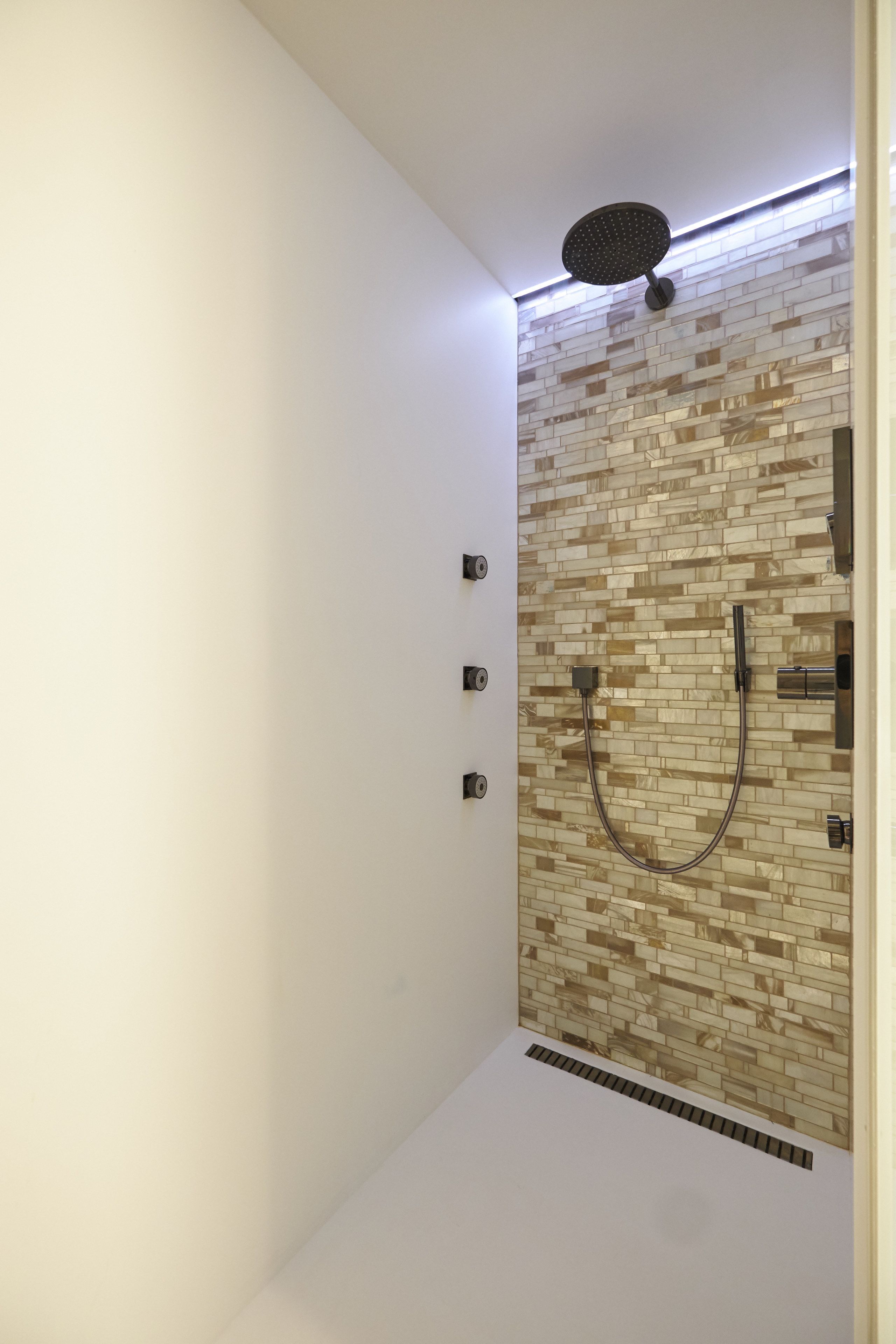A modern shower with a tiled wall and a handheld showerhead.