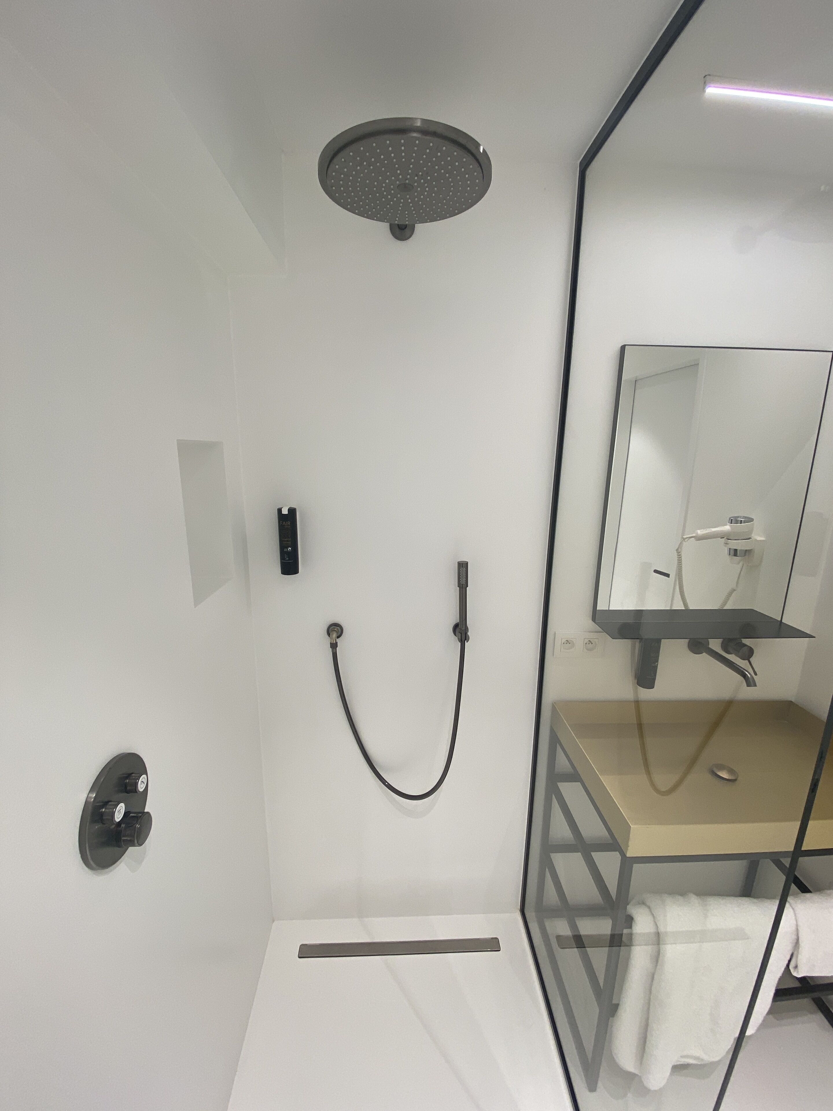 A modern bathroom with a glass shower enclosure, a sink with a mirror, and a towel rack.