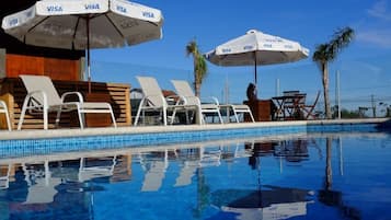 Una piscina al aire libre, sombrillas, sillones reclinables de piscina