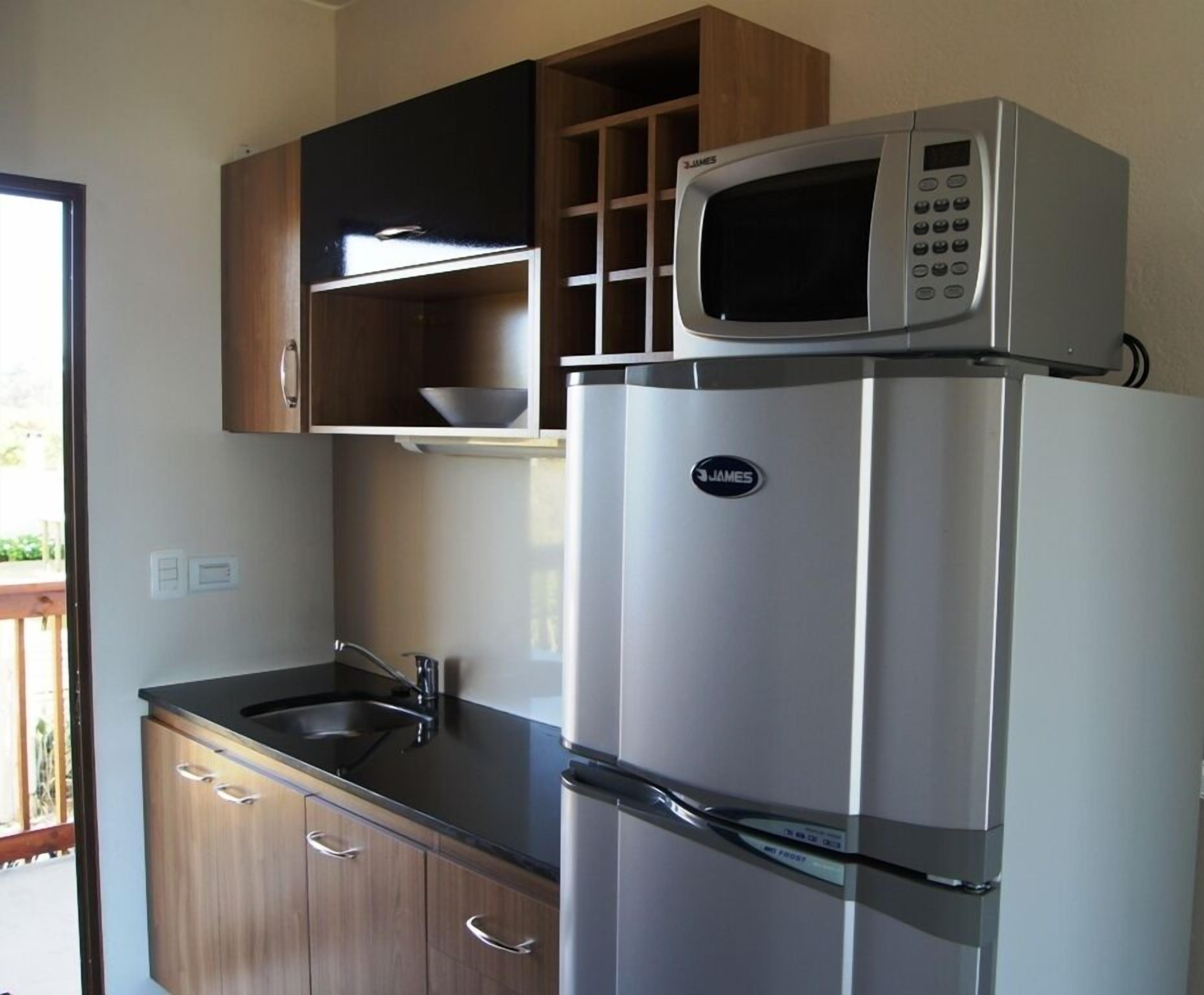 Una cocina compacta con un refrigerador de acero inoxidable, un microondas y armarios de madera.