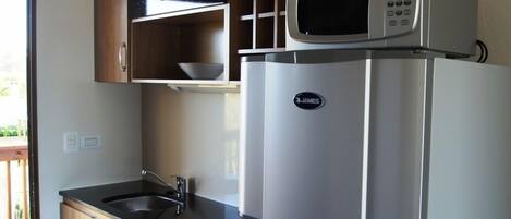 Una cocina compacta con un refrigerador de acero inoxidable, un microondas y armarios de madera.