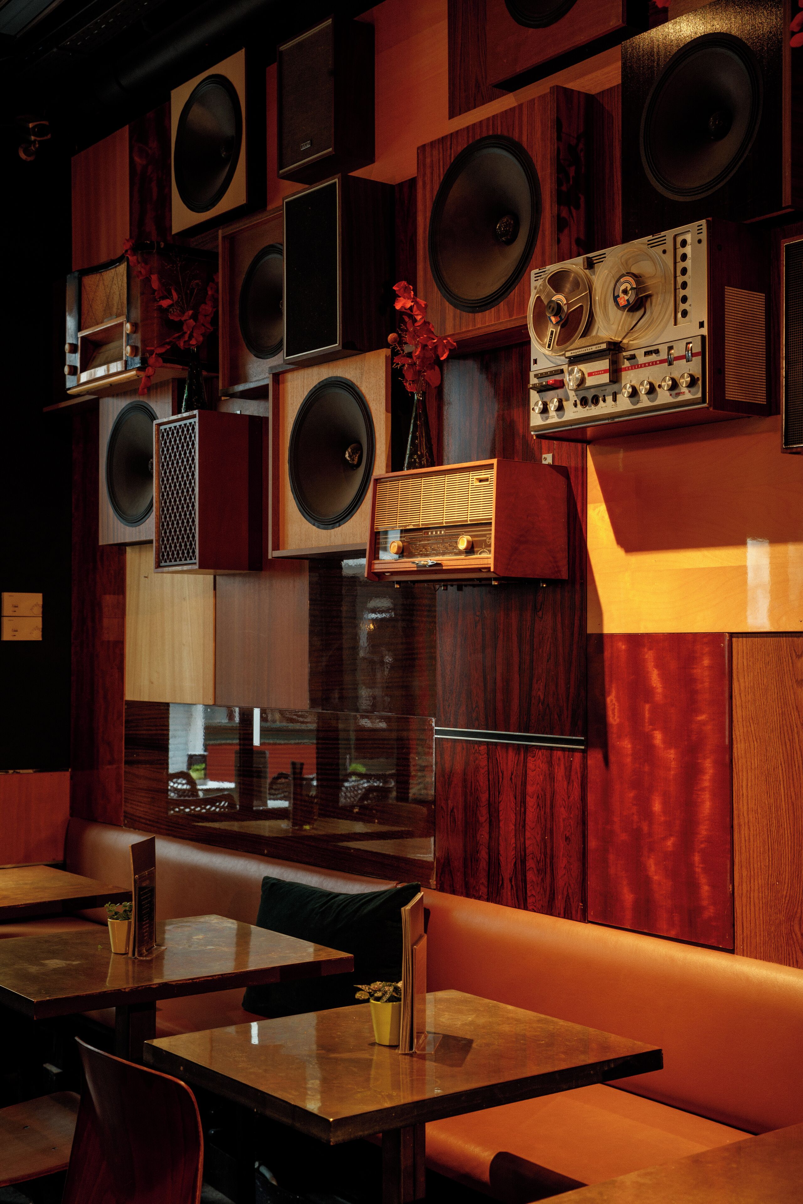 A restaurant interior with wooden paneling, multiple speakers, and a vintage radio. Tables and booths are available for seating.