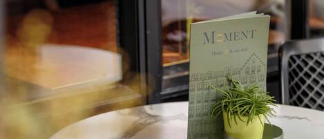 Une table ronde avec un présentoir à menus, une plante en pot et un menu intitulé « Moment Hotel Kathedraal ».