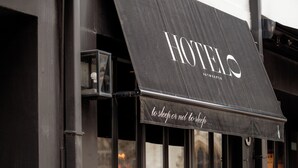 A hotel exterior with a black awning, outdoor seating with chairs and tables, and a window display of flowers. - HotelO Kathedral Antwerp (Antwerp)