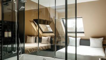 Ein modernes Hotelzimmer mit einer Glaskabinedusche, einem großen Bett und Blick auf die Stadt durch ein Fenster.