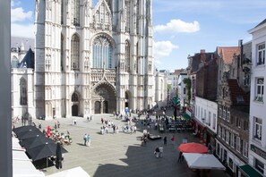 A cathedral with intricate Gothic architecture, a central courtyard with people and outdoor seating, and adjacent buildings with commercial establishments.