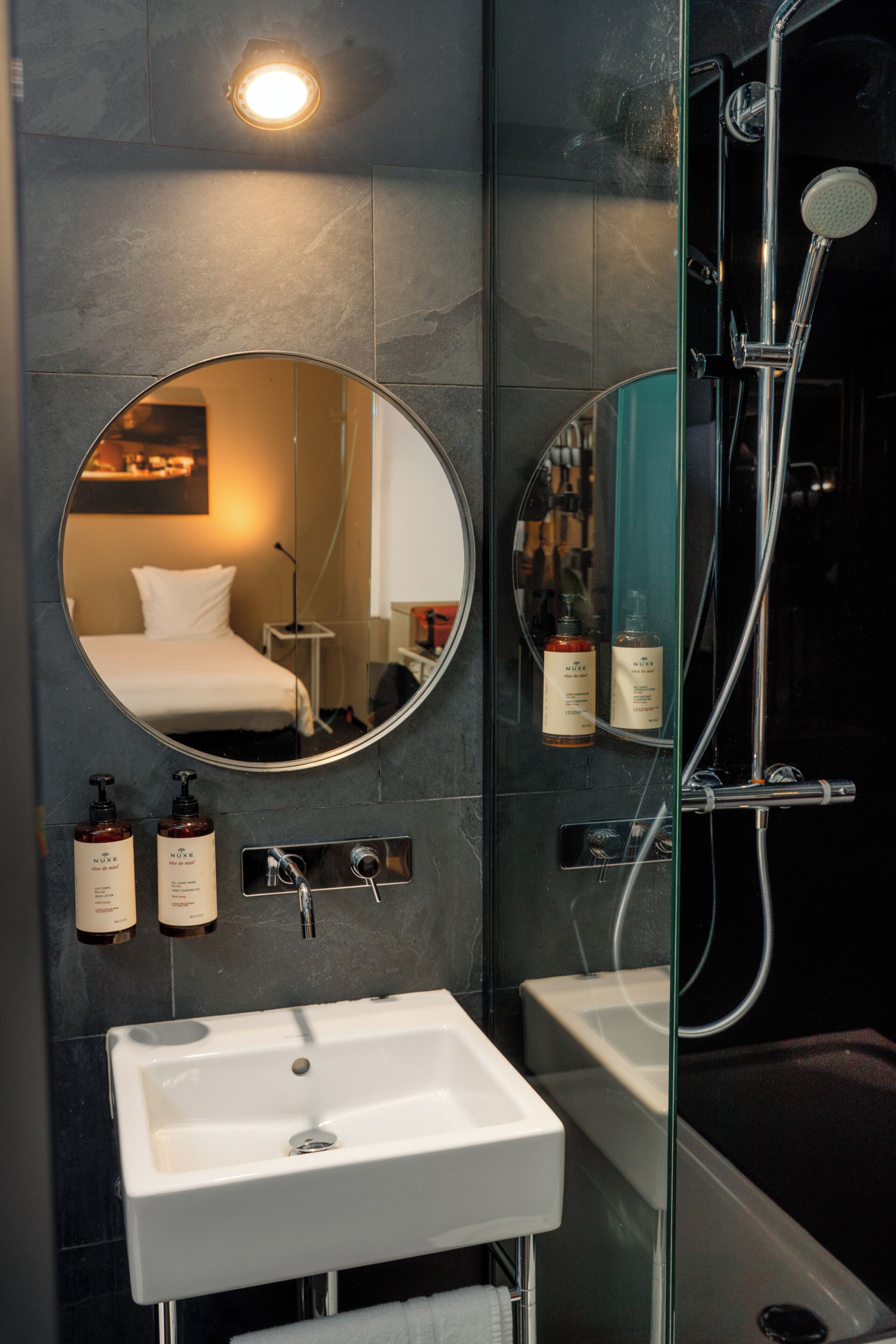 Ein modernes Badezimmer mit rundem Spiegel, Waschbecken in Weiß, Badewanne und Dusche.