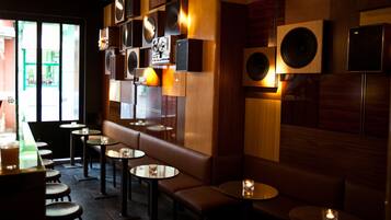 Interior de un restaurante con varias mesas y cabinas, paneles de madera y altavoces en la pared.